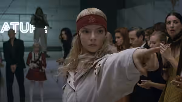Joan (Anya Taylor-Joy) points ahead amid a group of onlookers indoors