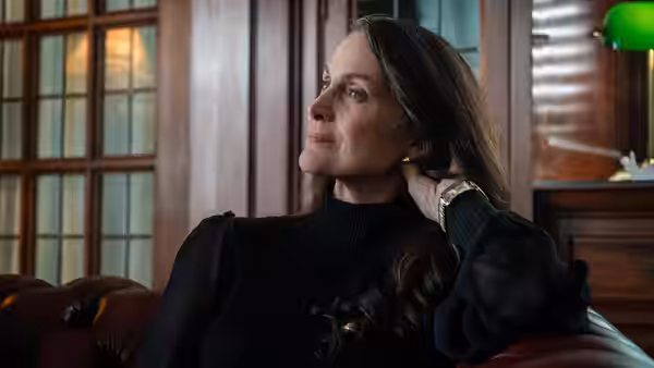 Katherine (Carrie-Anne Moss) sits on a sofa, touching her hair as she looks aside