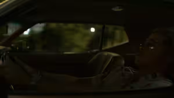 Cliff Booth (Brad Pitt) reclining behind the wheel of a car