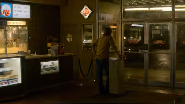 A man leans against a counter inside a dimly lit roadside diner