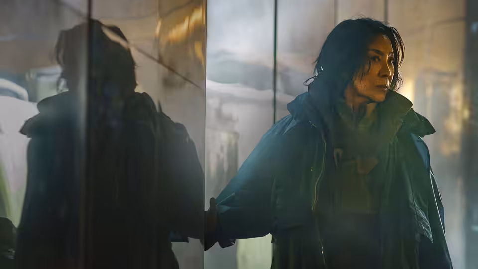 Olwen (Michelle Yeoh) standing with hand on glass in a foggy corridor