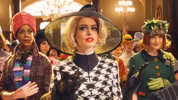 Grand High Witch (Anne Hathaway) with a cat surrounded by witches indoors