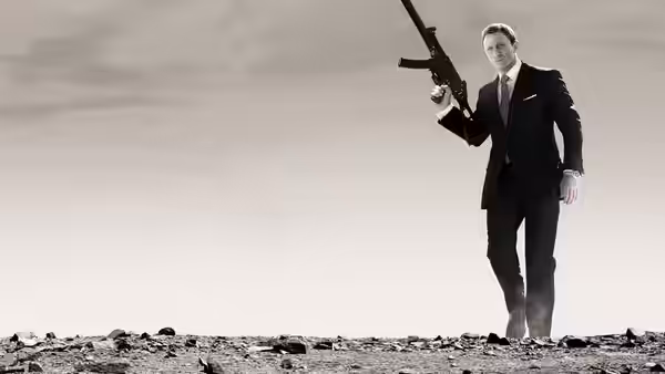 James Bond (Daniel Craig) walking with submachine gun raised in barren land