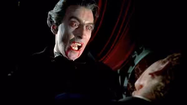 Count Dracula (Christopher Lee) leans over a woman beneath red curtains