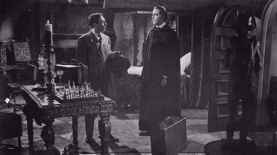 Doctor Van Helsing (Peter Cushing) stands with a man beside laboratory equipment