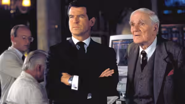 Pierce Brosnan as James Bond stands with arms crossed beside Desmond Llewelyn as Q