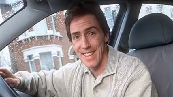 Keith (Rob Brydon) smiles from the driver's seat as rain falls outside