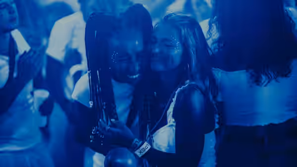 Two women hugging and smiling in a blue-lit party crowd