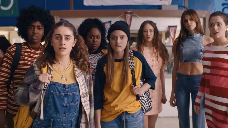 PJ (Rachel Sennott) and Josie (Ayo Edebiri) standing with girls in a school hallway