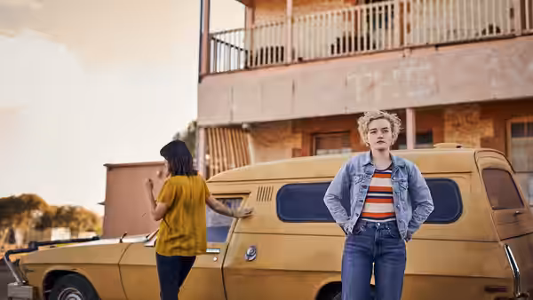 Hanna (Julia Garner) standing beside a yellow van outside a weathered building