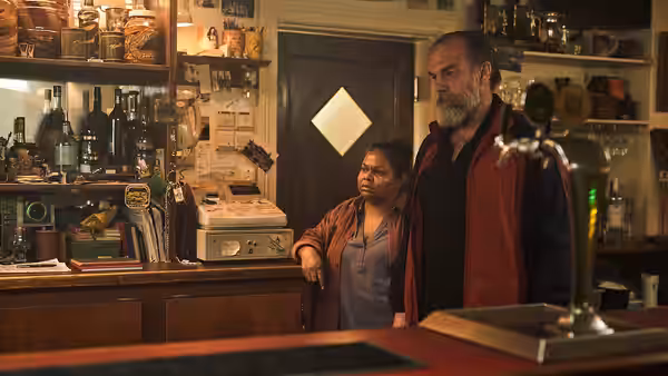 Billy (Hugo Weaving) and Carol (Ursula Yovich) standing behind a hotel bar