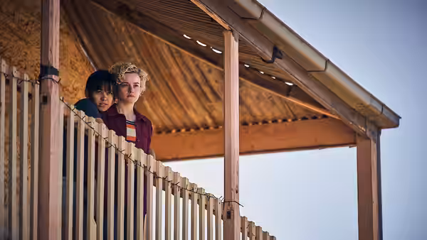 Hanna (Julia Garner) and Liv (Jessica Henwick) leaning on a wooden balcony railing