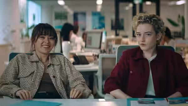 Liv (Jessica Henwick) and Hanna (Julia Garner) seated together at an office desk