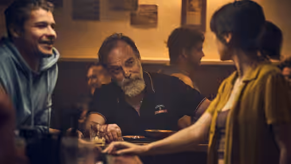 Billy (Hugo Weaving) seated at a table inside a crowded hotel bar