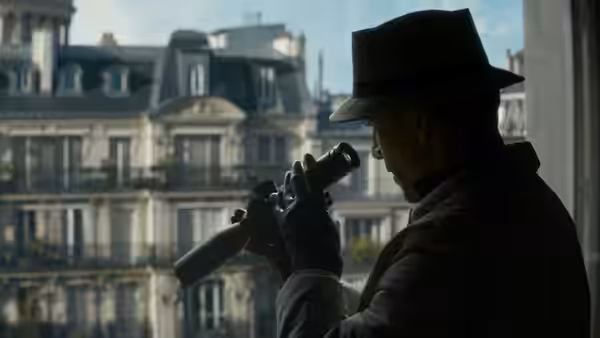 The Killer (Michael Fassbender) peering through binoculars from a window overlooking buildings