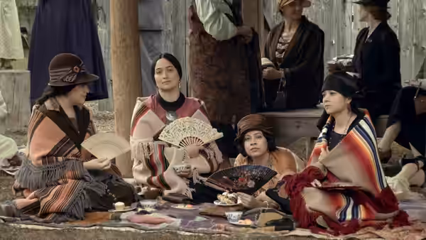 A group of women in shawls sitting on the ground holding fans