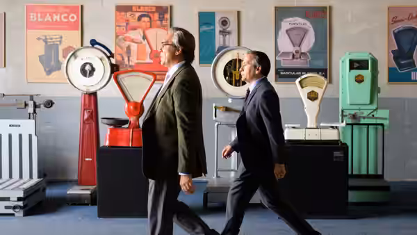 Julio Blanco (Javier Bardem) walking beside a colleague through the scale showroom