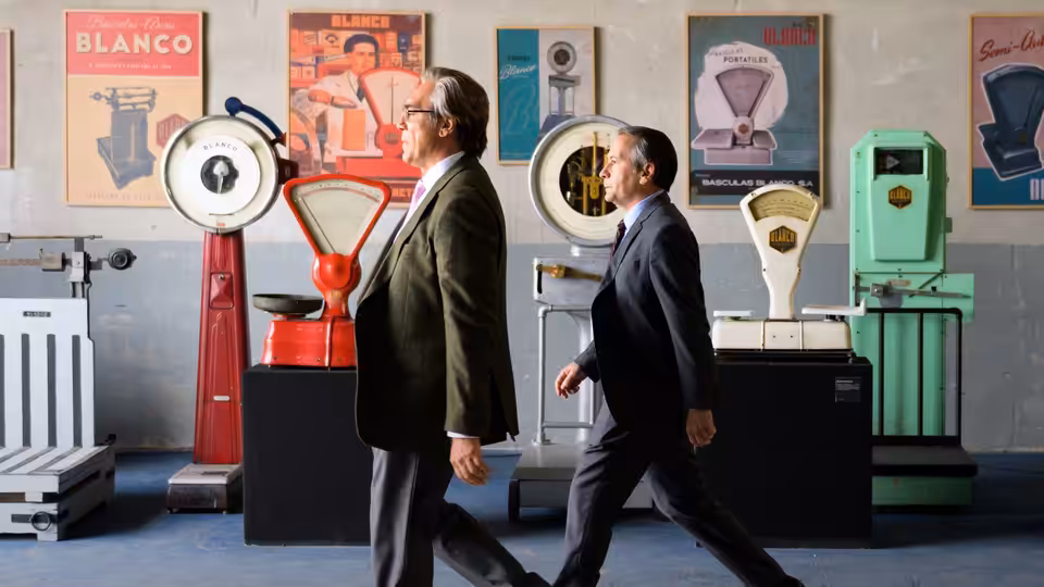 Julio Blanco (Javier Bardem) walking beside a colleague through the scale showroom
