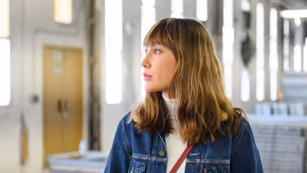 Liliana (Almudena Amor) standing in a bright factory corridor looking aside