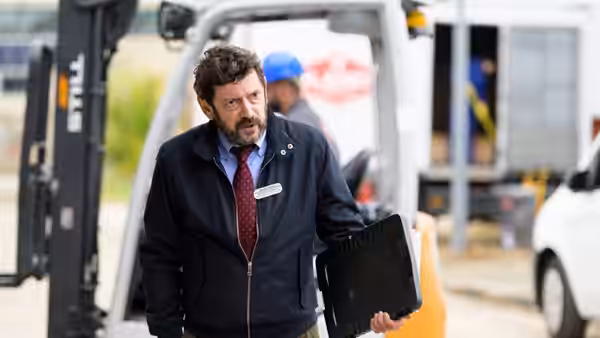A bearded man holding a clipboard beside a forklift at the loading area