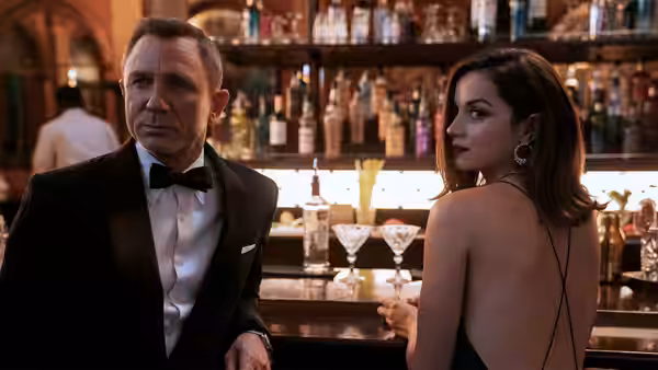 James Bond (Daniel Craig) standing at a bar beside a woman in black dress