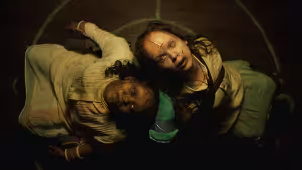 Two injured girls lie on wooden floor looking upward in darkness
