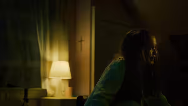 Young woman in green hoodie sits on floor in dimly lit bedroom