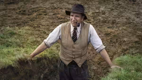 Basil Brown (Ralph Fiennes) stands on the grassy edge of an excavation