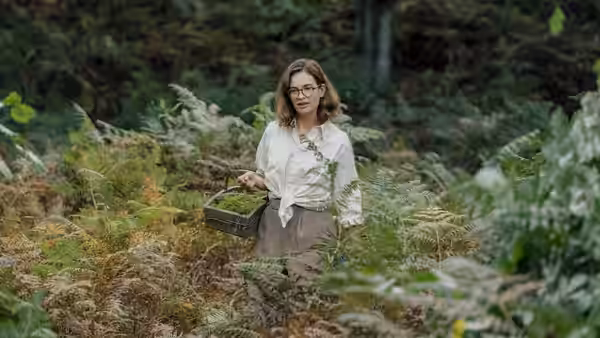 Peggy Piggott (Lily James) stands in a fern forest holding a basket
