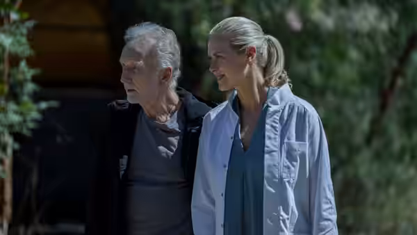 John Kramer (Tobin Bell) walking outdoors beside a smiling woman
