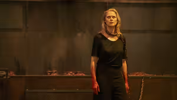 a bloodied woman standing in a dark industrial room with chains