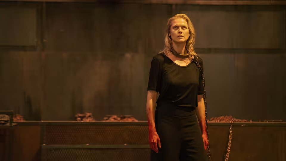 a bloodied woman standing in a dark industrial room with chains