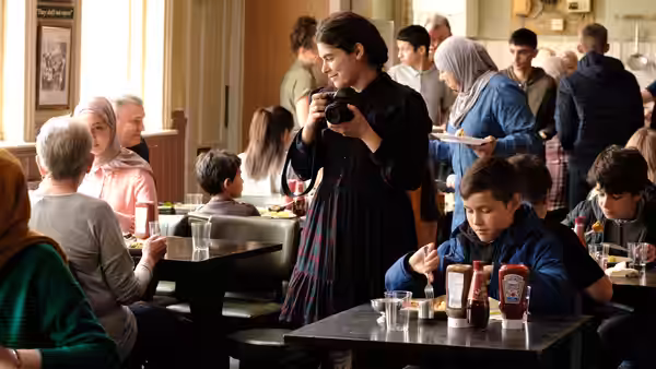 Yara (Ebla Mari) holds a camera among diners in a busy pub