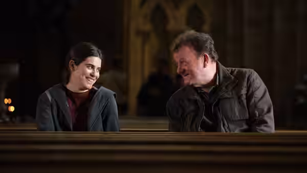 Yara (Ebla Mari) and TJ (Dave Turner) smile together in church pews