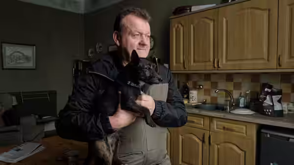 TJ (Dave Turner) holds a small dog inside his kitchen