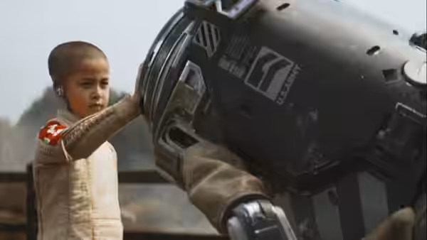 Alphie (Madeleine Yuna Voyles) touching large robotic vehicle