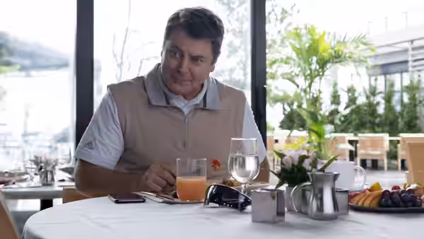 Ken Griffin (Nick Offerman) seated at a restaurant table with a drink