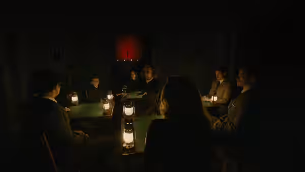 Group seated around a lantern-lit table in a dark hall