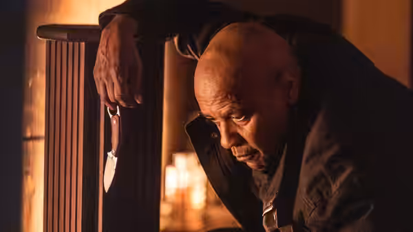 Robert McCall (Denzel Washington) leaning over a railing while holding a knife