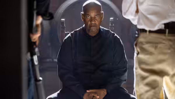 Robert McCall (Denzel Washington) seated with hands clasped in a dark space