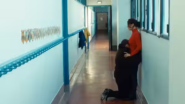 A woman in a red top embracing a kneeling man in a school corridor