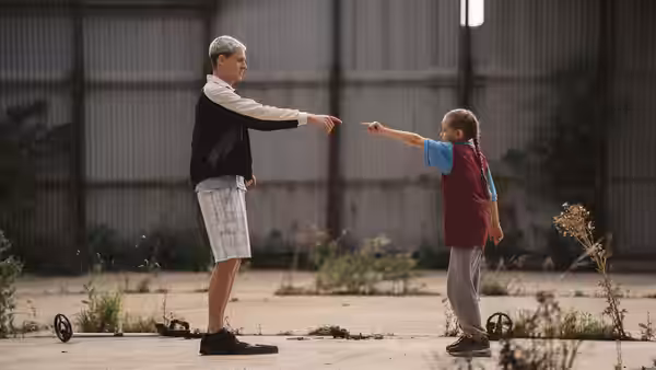 Jason (Harris Dickinson) and Georgie (Lola Campbell) pointing at each other in a yard