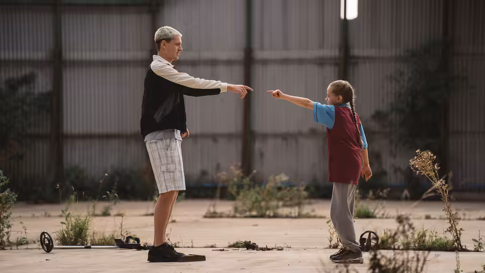 Jason (Harris Dickinson) and Georgie (Lola Campbell) pointing at each other in a yard