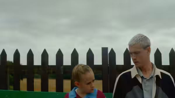 Georgie (Lola Campbell) and Jason (Harris Dickinson) standing by a wooden fence