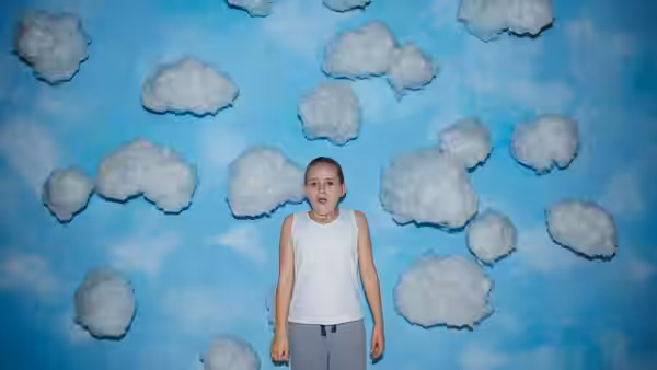 Georgie (Lola Campbell) standing before a blue wall with cotton clouds