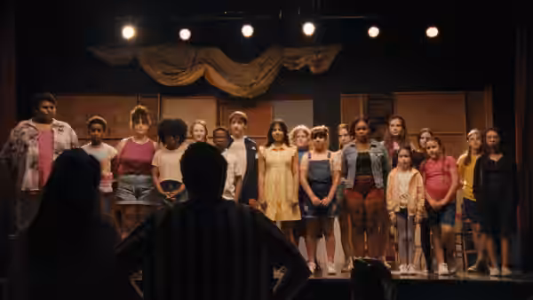 director facing a line of young performers standing on a theater stage