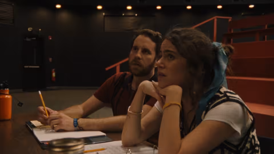 man writing at a table as a woman rests her chin on her hands