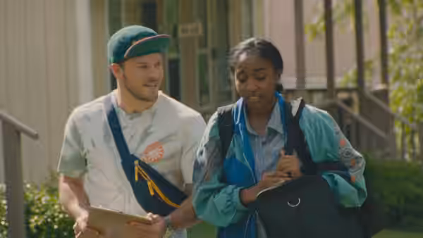 man holding a clipboard walking beside a woman checking her phone