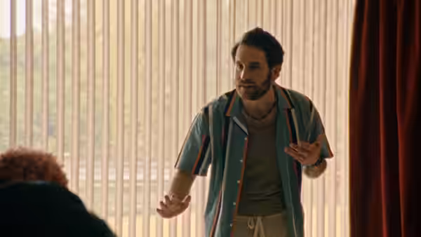 bearded man in a short-sleeved shirt gesturing while talking to someone