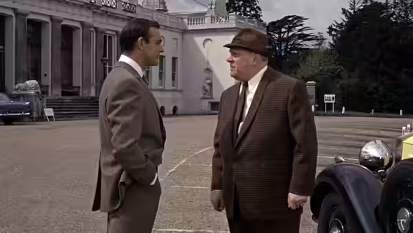 James Bond (Sean Connery) faces Auric Goldfinger (Gert Fröbe) outside a grand estate